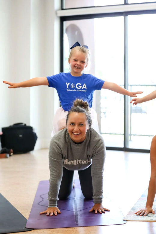 A child smiling on an adult shoulders during a playful yoga class