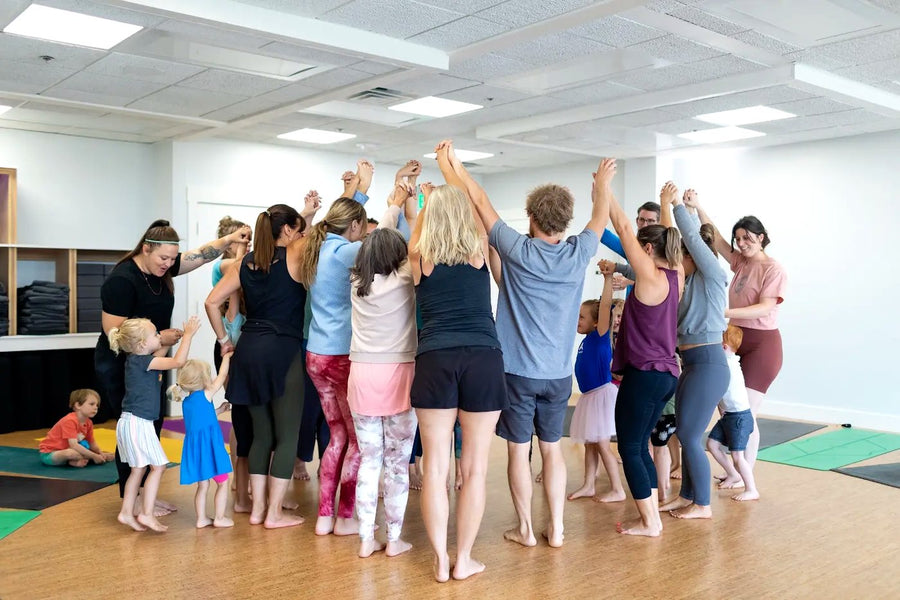 Rainbow Yoga trainees smiling and reaching up together in a bright group circle