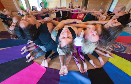 Rainbow Yoga trainees smiling together in a colourful human mandala circle