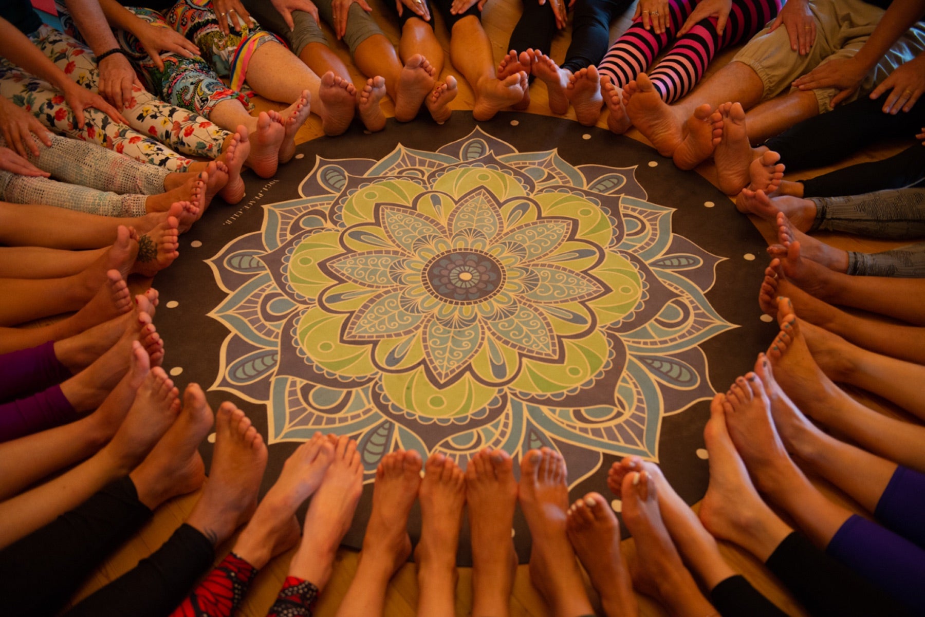 Rainbow Yoga trainees sitting in a colourful circle around a mandala mat