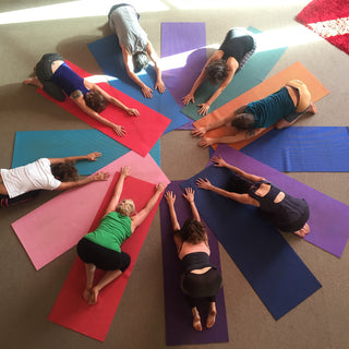 Rainbow Yoga trainees resting on colourful mats in a star-shaped group relaxation