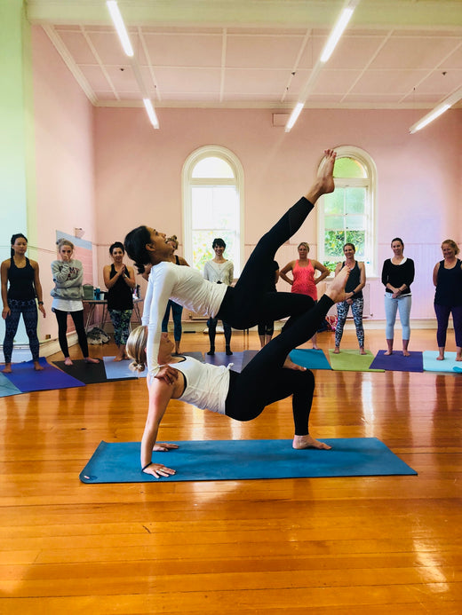 Rainbow Yoga trainees watching a joyful acro demonstration in a bright studio