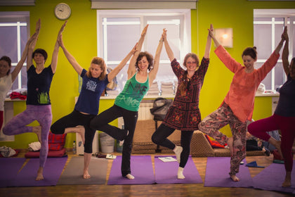 Rainbow Yoga trainees practising tree pose together in a bright green studio